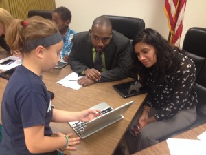 A female student shows 2 board members her computer program on a Chromebook