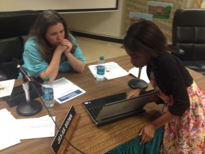 A board member looks on as a female student shows her project on a laptop